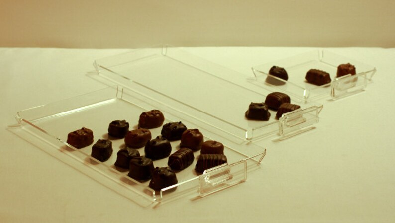 K&ouml;nnte beinhalten: Drei transparente Acryl-Tabletts mit Schokoladenbonbons auf dem oberen Tablett. Die Tabletts sind &uuml;bereinander gestapelt.