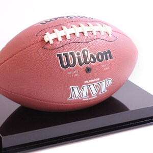 May include: A brown leather Wilson MVP football with white laces, displayed on a black rectangular stand. The football has the Wilson logo and the text "MVP" printed on it. The football is inflated to 7-9 lbs.