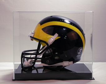 May include: A black and yellow football helmet with a clear face mask is displayed inside a clear acrylic case. The helmet has a yellow stripe and the Schutt logo. The case sits on a black base.