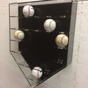 K&ouml;nnte beinhalten: Ein schwarzer Baseball-Pr&auml;sentationskasten aus Acryl mit f&uuml;nf wei&szlig;en Baseballs mit roten N&auml;hten. Der Kasten hat f&uuml;nf Regale und ist in Form eines Baseball-Diamanten.