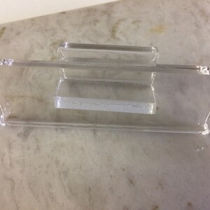 K&ouml;nnte beinhalten: Ein transparenter Handyst&auml;nder aus Kunststoff mit einer erh&ouml;hten Plattform zum Halten eines Telefons.