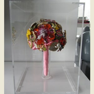 May include: A clear acrylic box with a pink ribbon bouquet made of various colorful brooches, rhinestones, and other jewelry.