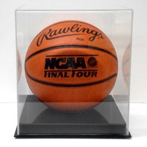 May include: A brown leather basketball with "Rawlings" and "NCAA Final Four" printed on it, displayed in a clear acrylic case with a black base.