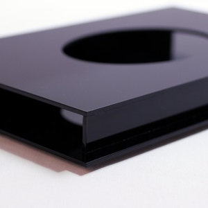 May include: A glossy black rectangular object with a circular cutout. The object has a sleek, modern design and appears to be made of a solid, reflective material. The edges are sharp and well-defined, creating a minimalist aesthetic.