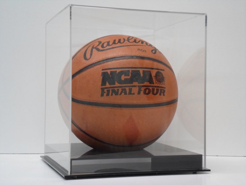 May include: A brown leather basketball with black markings, including the text "Rawlings" and "NCAA Final Four", displayed in a clear acrylic display case with a black base.