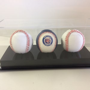 May include: Three baseballs in a clear acrylic display case. The middle baseball has a Detroit Tigers logo. The case has a black base.