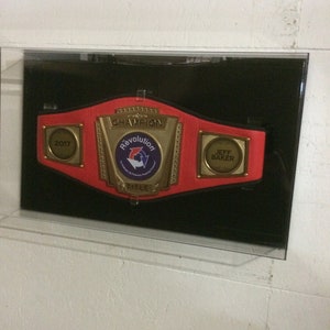 May include: A red and gold championship belt with the words "Champion" and "Revolution Title" on it. The belt has a 2017 date plate and a plate that says "Jeff Baker".
