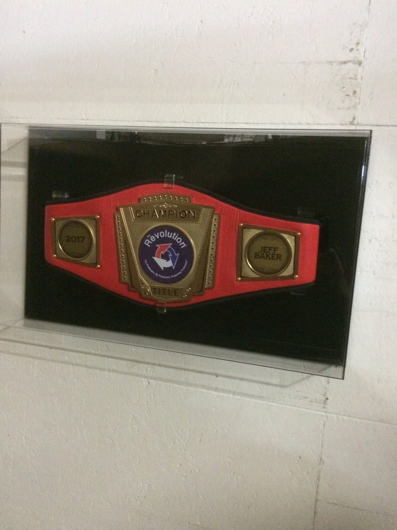 May include: A red and gold championship belt with the words "Champion" and "Revolution Title" on it. The belt has a 2017 date plate and a plate that says "Jeff Baker".
