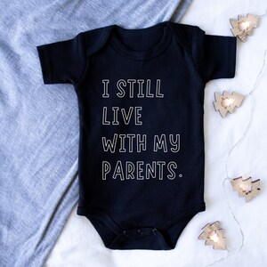 May include: Black baby onesie with white text that reads "I still live with my parents."