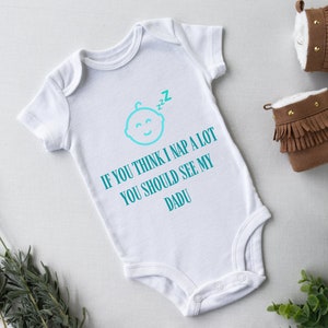 May include: White baby onesie with a turquoise blue graphic of a sleeping baby with the text "If you think I nap a lot you should see my DADU".