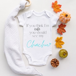 May include: White baby onesie with the text "If you think I'm cute you should see my Chachu" in gray and blue lettering. The onesie is surrounded by fall-themed decorations, including small pumpkins, pinecones, and fall leaves.