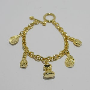 May include: A gold chain bracelet with multiple charms. The charms are shaped like leaves and bags. The bracelet has a toggle clasp.