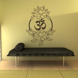 May include: A brown wall decal with an Om symbol surrounded by stylized flowers in a circle. The decal is on a light yellow wall above a black futon.