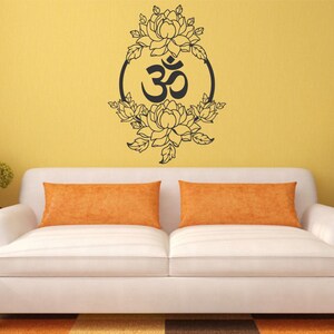 May include: A white couch with two orange pillows in front of a yellow wall with a black and white wall decal of an Om symbol surrounded by flowers.