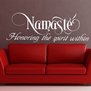 May include: White vinyl wall decal with the text "Namaste" in a decorative font and the phrase "Honoring the spirit within" below it. The decal is on a gray wall behind a red couch.