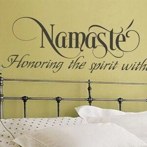 May include: A wall decal with the word "Namaste" in a decorative font, with the phrase "Honoring the spirit within" below it. The decal is above a bed with white bedding.
