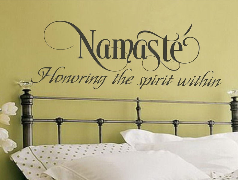 May include: A wall decal with the word "Namaste" in a decorative font, with the phrase "Honoring the spirit within" below it. The decal is above a bed with white bedding.