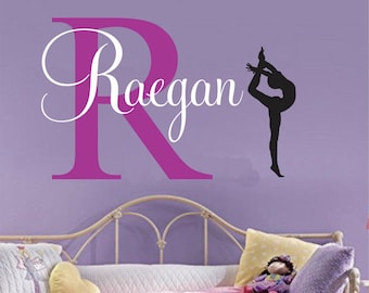 May include: A pink and white wall decal with the name "Raegan" and a silhouette of a gymnast in a backbend pose.