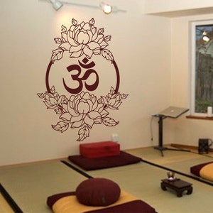 May include: A brown wall decal with a floral design surrounding the Om symbol. The decal is on a wall in a room with a wooden floor and two brown cushions.