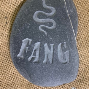 Piedra de memoria tallada a mano que incluye el nombre de su ser querido, con la silueta de una serpiente encima.