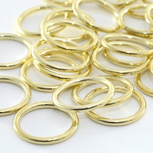 Könnte beinhalten: Ein Haufen goldfarbener Metallringe. Die Ringe sind alle gleich groß und gleich geformt und in einem zufälligen Muster angeordnet.