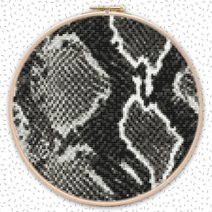 Könnte beinhalten: Ein schwarzes und weißes Kreuzstich-Design mit Schlangenhautmuster in einem hölzernen Stickrahmen.