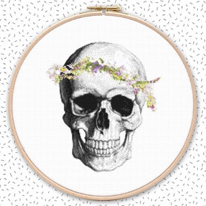 May include: A black and white illustration of a human skull with a floral wreath around its head. The flowers are in shades of purple, pink, and yellow.