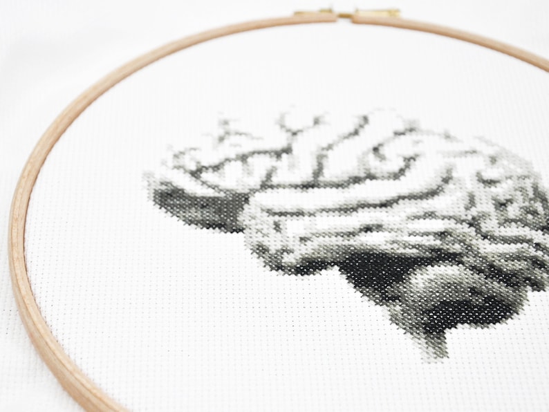 May include: A black and white cross-stitch embroidery of a human brain on white fabric in a wooden embroidery hoop.
