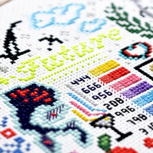 Könnte beinhalten: Eine bunte Kreuzstich-Stickerei mit verschiedenen Symbolen und Designs, darunter eine Wolke, ein Herz, eine Blume und ein Regenbogen. Die Stickerei enthält auch den Text "A Year of 12".