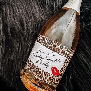 Puede incluir: Una botella de champ&aacute;n con una etiqueta de estampado de leopardo que dice "Jenna's Bachelorette Party" con una marca de beso de l&aacute;piz labial rojo.