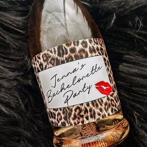 Puede incluir: Una botella de vidrio transparente con una etiqueta de estampado de leopardo que dice "Jenna's Bachelorette Party" con una marca de beso de l&aacute;piz labial rojo.