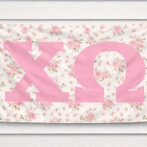 May include: A rectangular banner with a floral pattern of pink roses on a white background. Large pink Greek letters, Chi and Omega, are prominently displayed on the banner, creating a decorative piece.