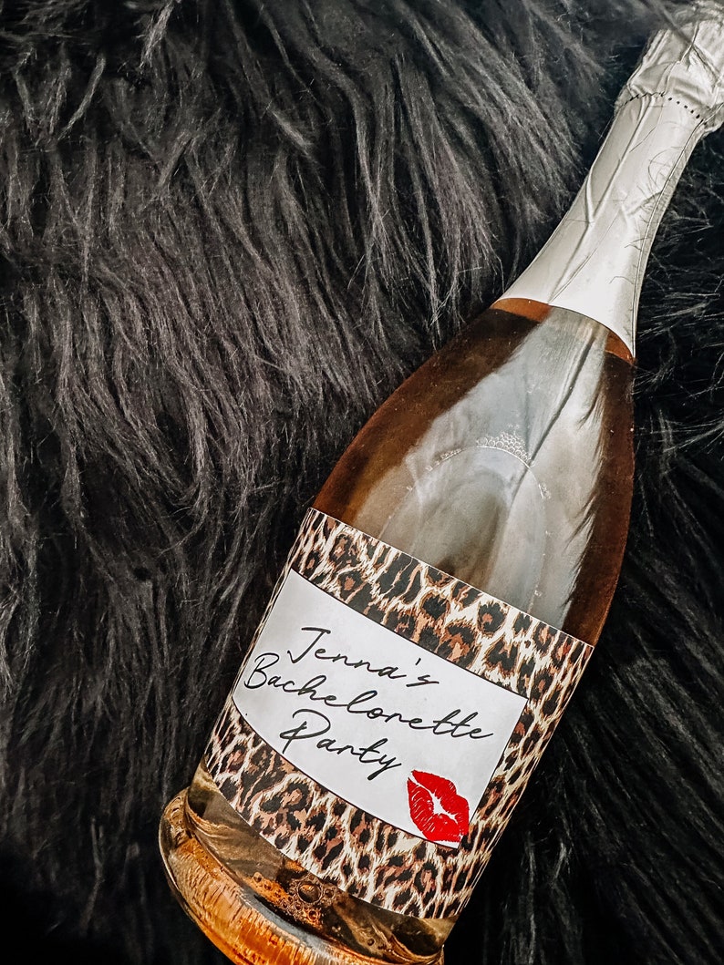 Puede incluir: Una botella de champ&aacute;n con una etiqueta de estampado de leopardo que dice "Jenna's Bachelorette Party" con una marca de beso de l&aacute;piz labial rojo.