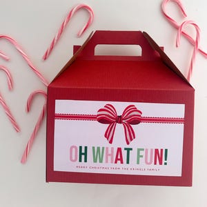 May include: Red gift box with a white label that says "Oh What Fun! Merry Christmas from the Kringle Family". The label has a red and white striped bow with a white background. The box is surrounded by candy canes.