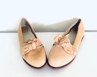 Puede incluir: Un par de zapatos de cuero beige de vestir con un lazo en la parte delantera.