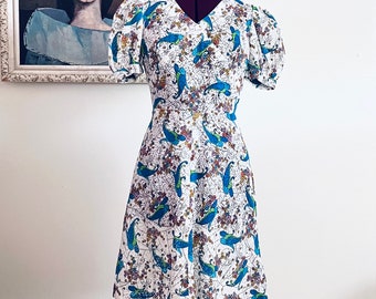 May include: A white dress with a blue and green floral pattern. The dress has a v-neck, short puff sleeves, and a flared skirt.