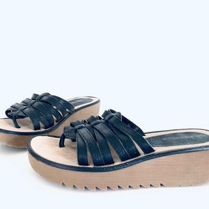May include: A pair of black leather wedge sandals with a woven strap design. The sandals have a light brown platform and a textured sole.