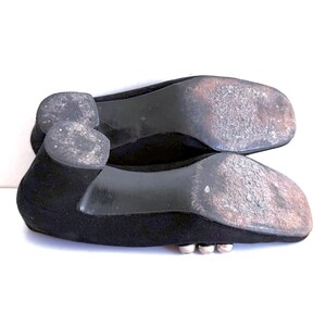 Op de afbeelding: Een paar zwarte platte schoenen, gezien vanaf de zolen, met slijtage. De schoenen hebben een lage hak en een eenvoudig ontwerp. De zolen vertonen gebruikssporen.