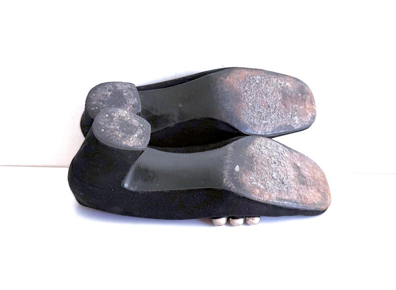 Op de afbeelding: Een paar zwarte platte schoenen, gezien vanaf de zolen, met slijtage. De schoenen hebben een lage hak en een eenvoudig ontwerp. De zolen vertonen gebruikssporen.