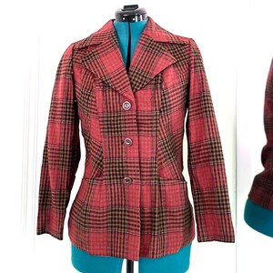 May include: A red and brown plaid blazer with a button closure. The blazer has a collar and long sleeves.