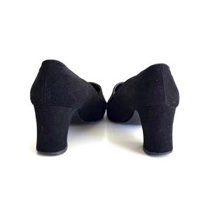 Op de afbeelding: Een paar zwarte su&egrave;de schoenen met hakken. De schoenen hebben een ronde neus en een blokhak. De hakken zijn ongeveer 7,6 cm hoog. De schoenen staan tegen een witte achtergrond.