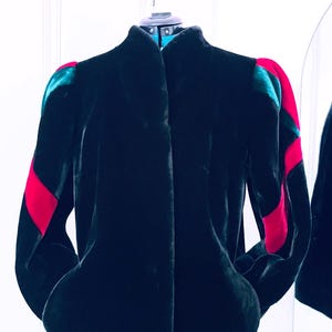 May include: A black faux fur jacket with red and green velvet accents on the sleeves. The jacket has a mandarin collar and a zipper closure.