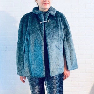 May include: A blue faux fur cape with a silver clasp closure. The cape is knee-length and has a collar.