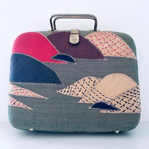 May include: A vintage green fabric suitcase with a brass handle and clasp. The suitcase is decorated with a patchwork design of different coloured fabrics, including red, brown, black, and beige.