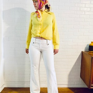 May include: A woman wearing a yellow button-down shirt with a knotted front, white pants, and a colorful headscarf.