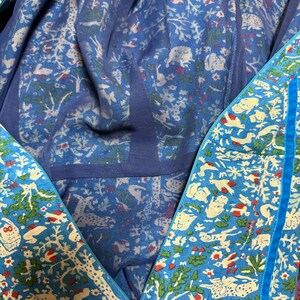 May include: A blue garment with a detailed pattern of white animals, trees, and red accents. The garment has a zipper and a blue trim. The inner lining is a lighter shade of blue with a similar pattern.