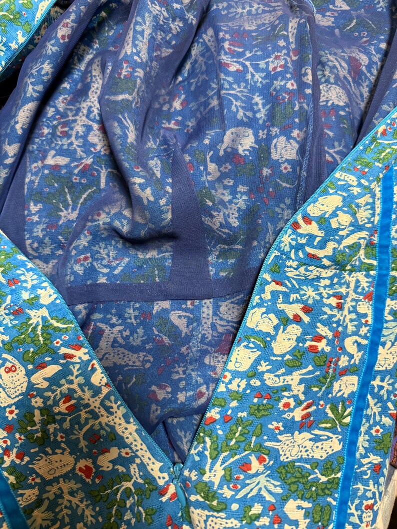 May include: A blue garment with a detailed pattern of white animals, trees, and red accents. The garment has a zipper and a blue trim. The inner lining is a lighter shade of blue with a similar pattern.