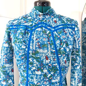 May include: A blue patterned dress with a high collar and long sleeves. The fabric features a white, red, and green forest design. The dress is accented with blue velvet trim.