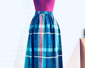 Puede incluir: Una falda de cuadros azules, blancos y rojos con silueta acampanada. La falda está hecha de una tela texturizada y tiene una cintura alta.