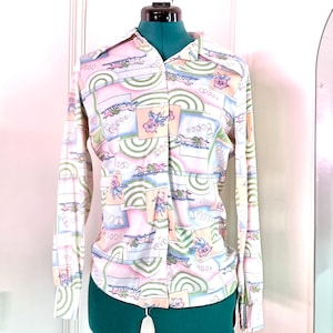 Peut inclure: Chemise à manches longues avec un motif abstrait coloré. Le col est classique. Le motif comprend des formes géométriques et des motifs floraux dans des tons de rose, bleu, vert et blanc. La chemise est boutonnée.